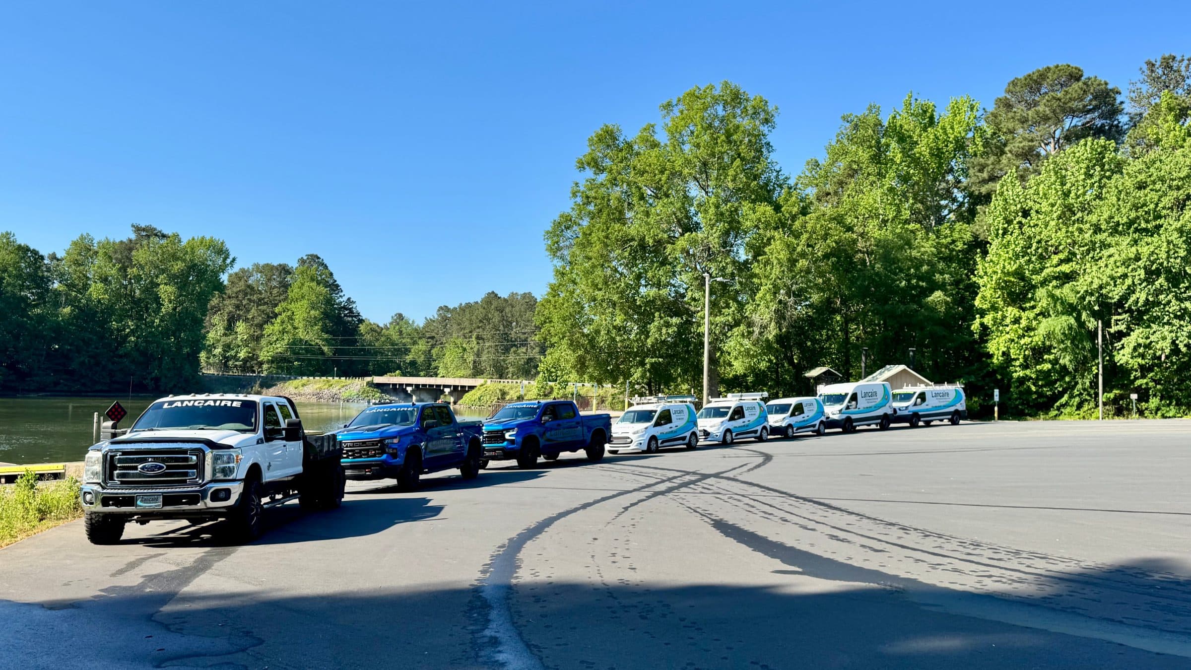 The Lancaire fleet — three branded trucks and five service vans lined up by the water.